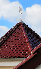 Detail einer Dachspitze mit roten Ziegeln und Wetterfahne